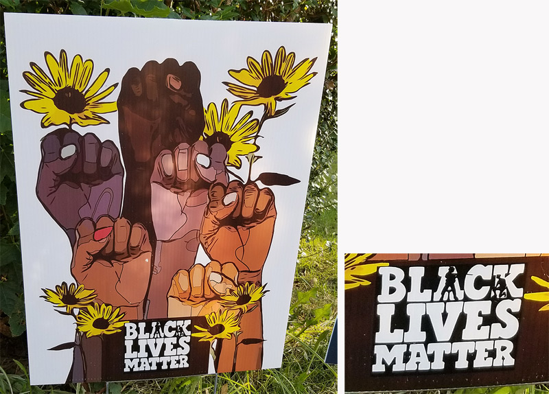 "Black Lives Matter" yard sign. Inside the the word "Black," the silhouette of a man, presumably a police officer, points a gun at a kneeling man.